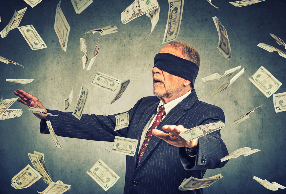 Blindfolded senior businessman trying to catch dollar bills banknotes flying in the air on gray wall background. Financial corporate success or crisis challenge concept-1